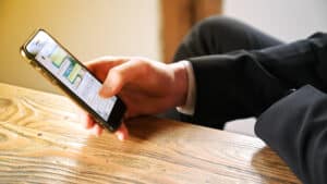 Businessman using digital smartphone on chat messenger - Krypto Investigation - Krypto Investigation Businessperson in a suit scrolling on a smartphone resting on a wooden table
