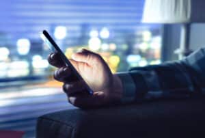 Phone with fraud text message unknown scam call or night texting Man using smartphone Anonymous caller or sms scammer Cheater with secret dating Light from cellphone screen in dark home - Krypto Investigation - Krypto Investigation Close-up of a hand holding a smartphone with blurred city lights in the background, at night